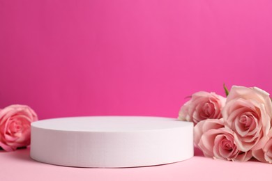 Photo of Stylish presentation for product. Round podium and beautiful roses against pink background, space for text