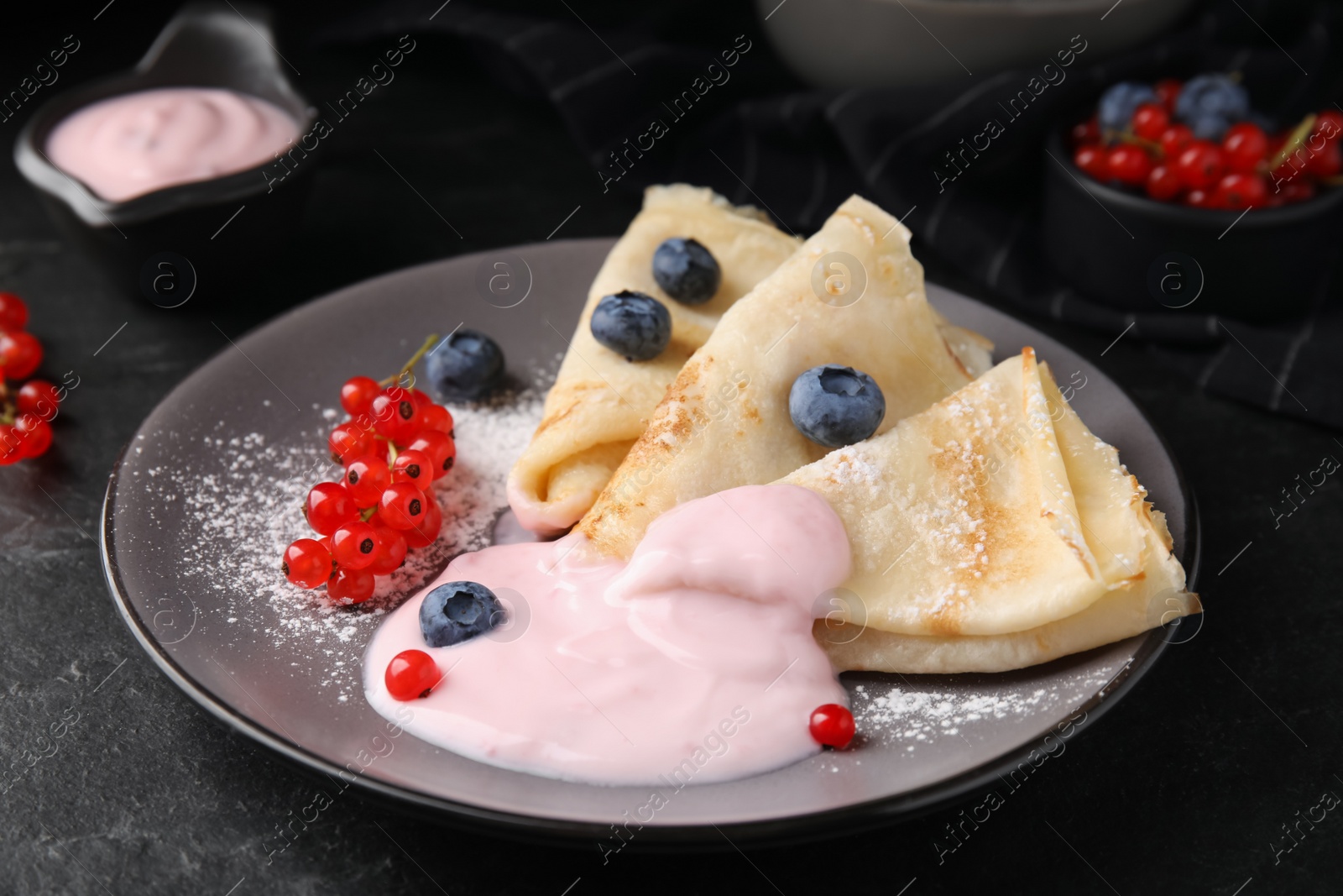 Photo of Delicious crepes with natural yogurt, blueberries and red currants on dark grey table