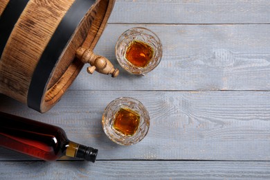 Photo of Barrel with tap, bottle and tasty whiskey on light gray wooden table, flat lay. Space for text