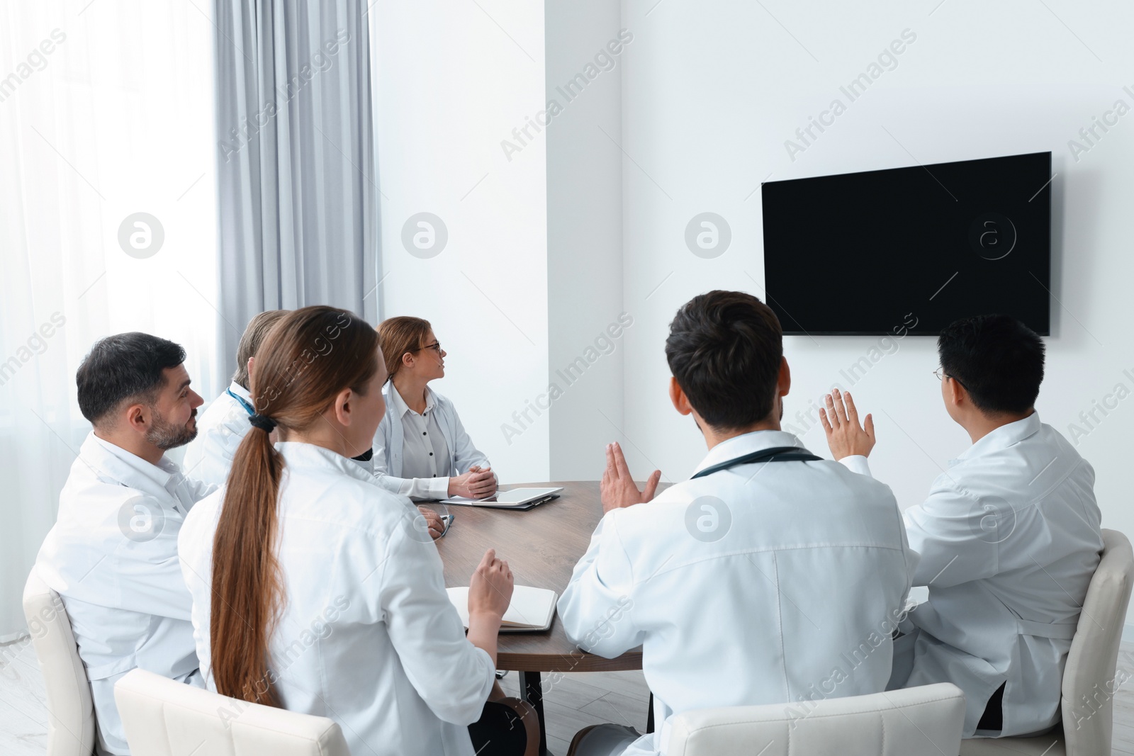 Photo of Team of doctors watching presentation on tv screen in room. Medical conference