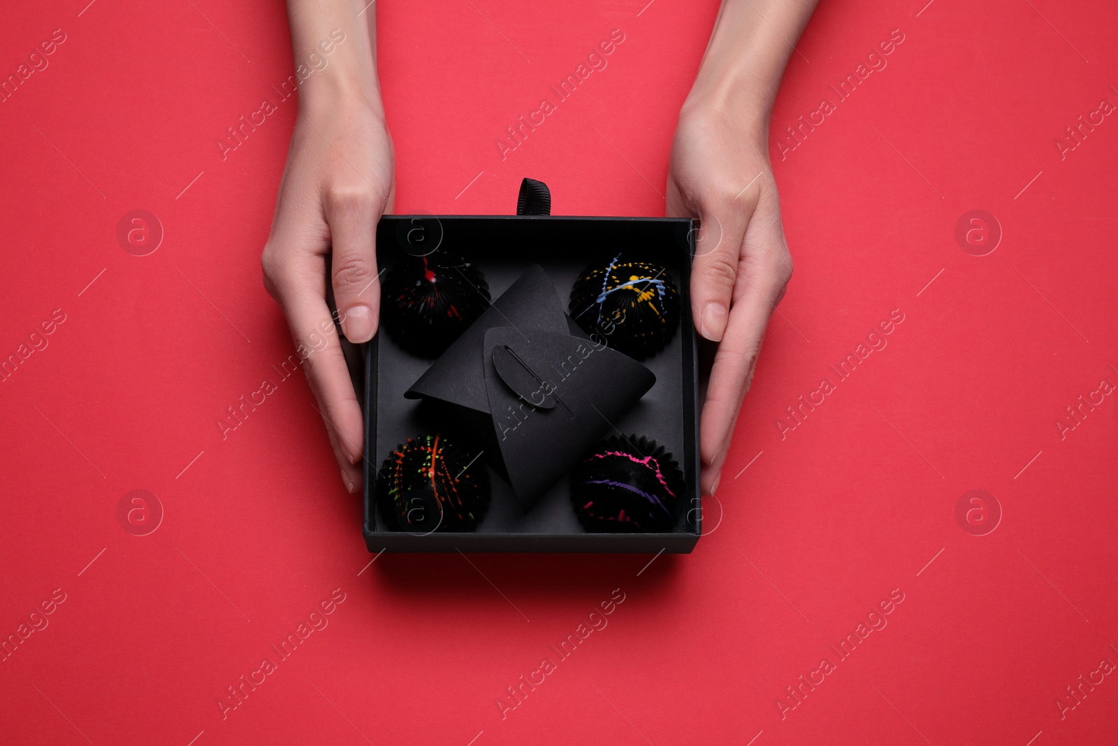 Photo of Woman with box of delicious chocolate candies on red background, top view