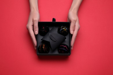 Woman with box of delicious chocolate candies on red background, top view