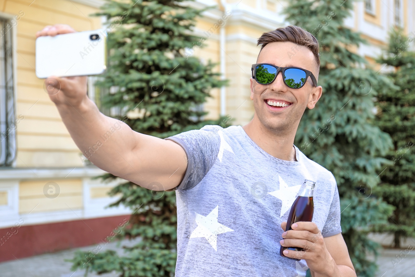 Photo of Young man with bottle of cola taking selfie outdoors