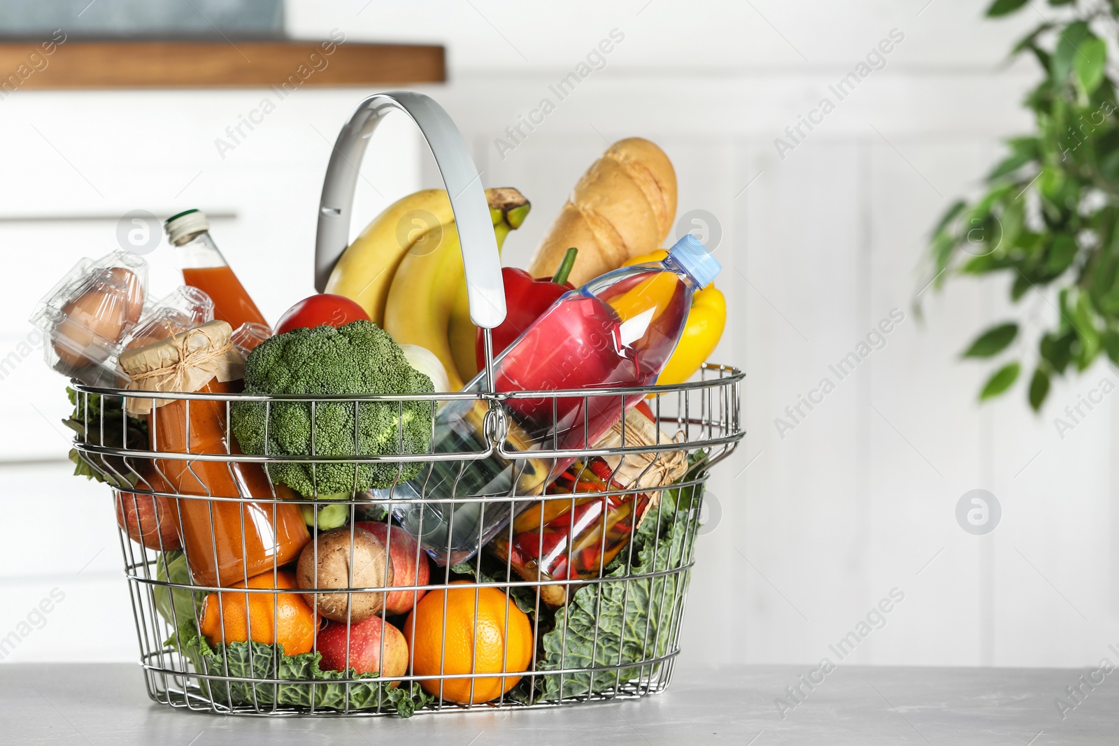 Photo of Shopping basket with grocery products on grey table indoors. Space for text