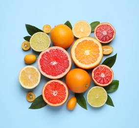 Photo of Fresh juicy citrus fruits with green leaves on light blue background, flat lay