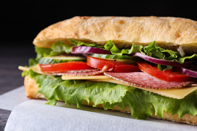 Delicious sandwich with fresh vegetables and salami on table, closeup