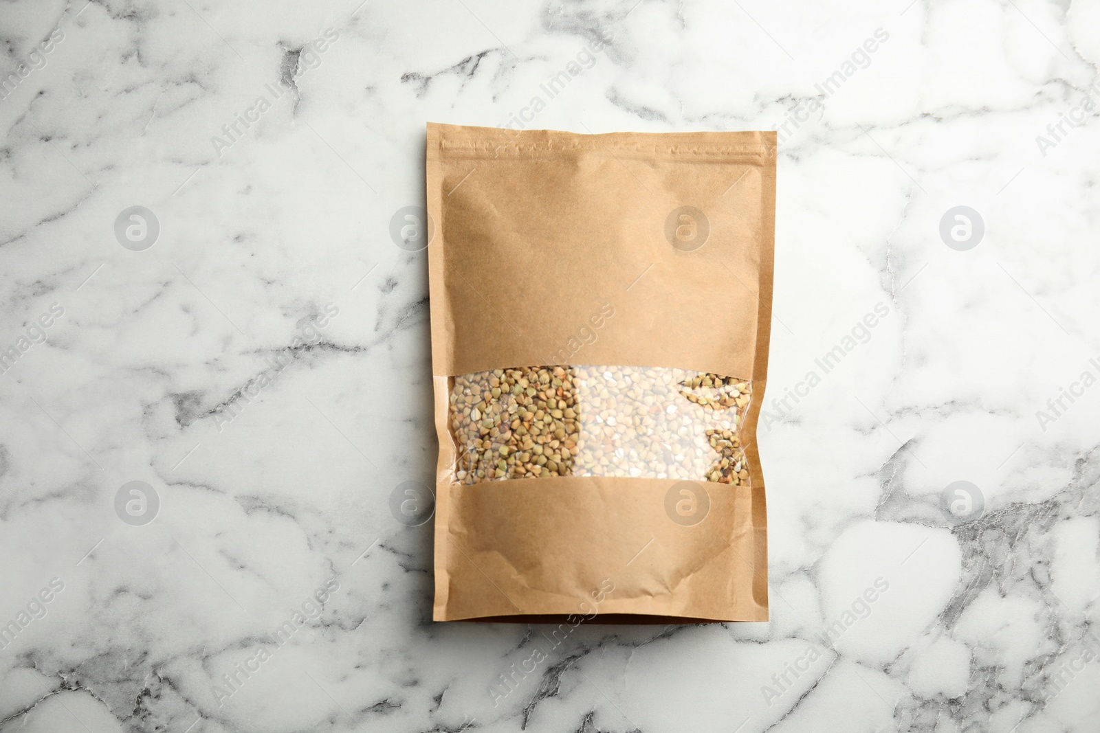 Photo of Uncooked green buckwheat grains in package on white marble table, top view. Space for design