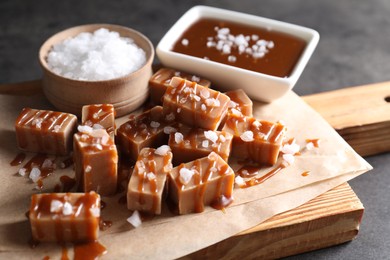 Tasty candies, caramel sauce and salt on grey table, closeup