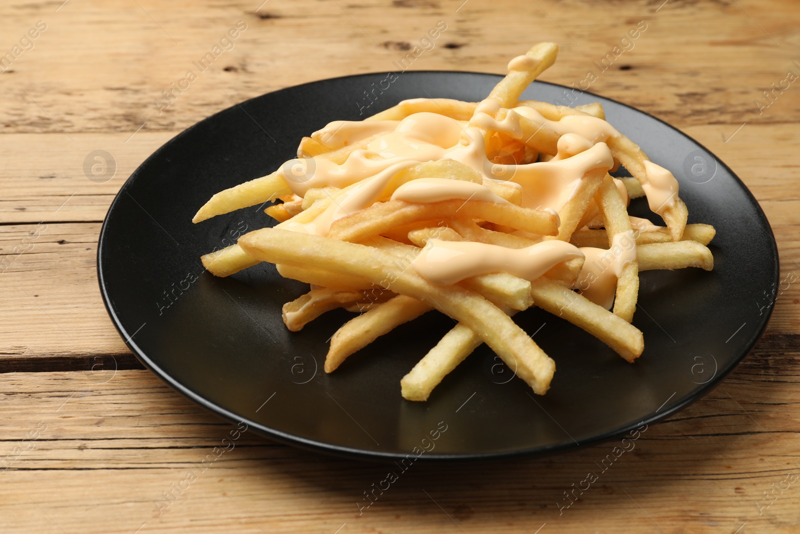 Photo of Delicious French fries with cheese sauce on wooden table, closeup