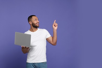 Smiling young man with laptop on lilac background, space for text