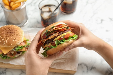 Photo of Woman holding tasty burger with bacon at served table, closeup