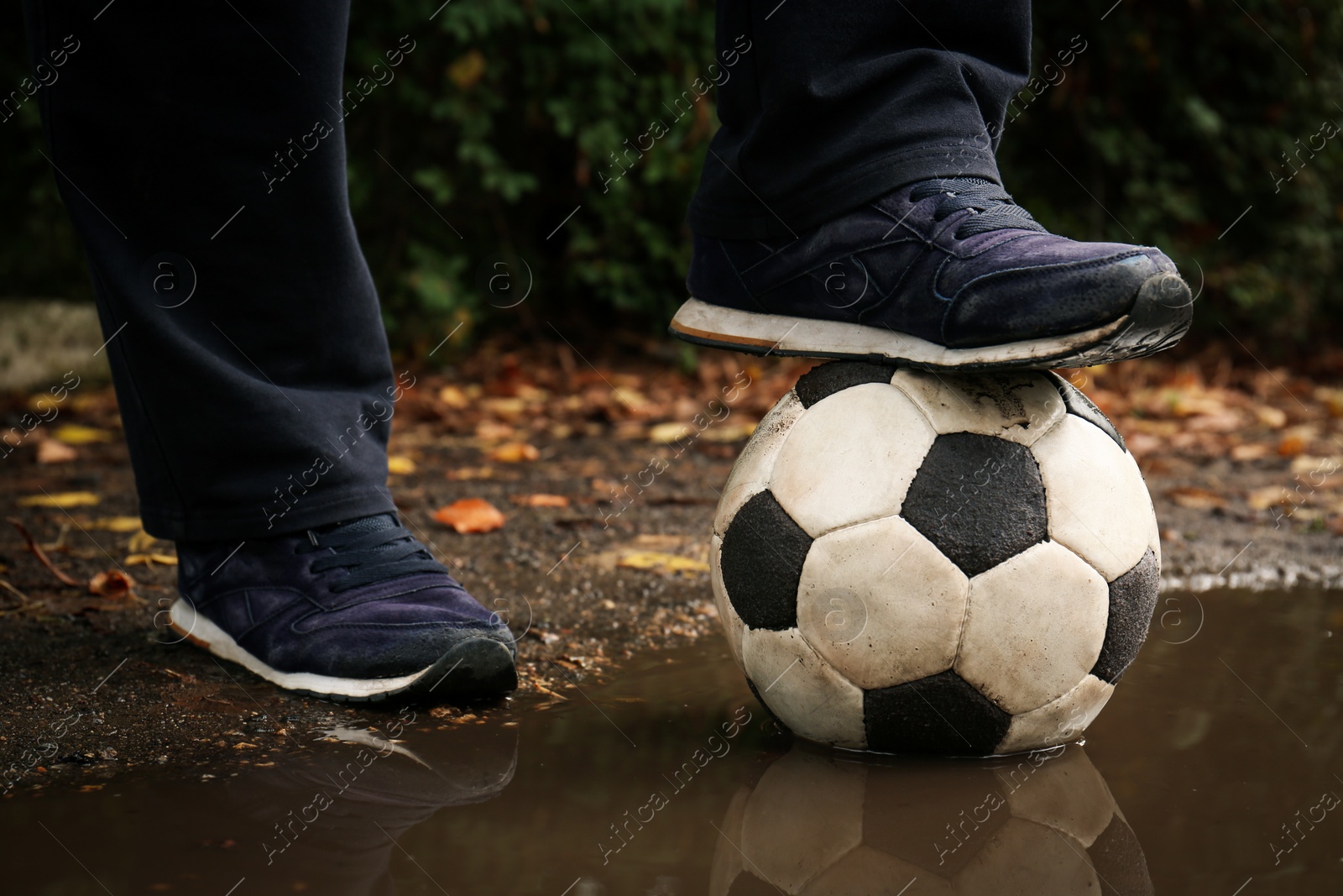 Photo of Man with soccer ball in muddy puddle outdoors, closeup