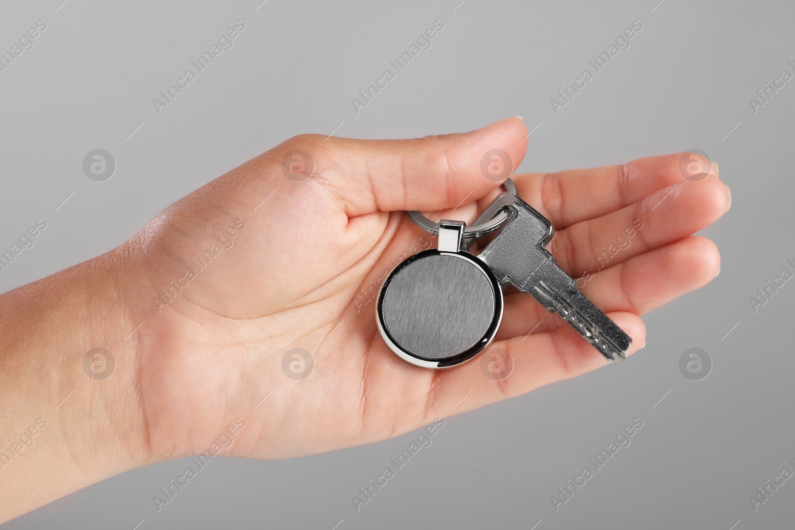 Photo of Woman holding key with metallic keychain on grey background, closeup