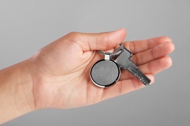 Woman holding key with metallic keychain on grey background, closeup