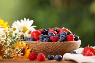 Photo of Bowl with different fresh ripe berries and beautiful flowers on table outdoors