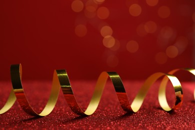 Photo of Shiny golden serpentine streamer on red table against blurred lights, closeup