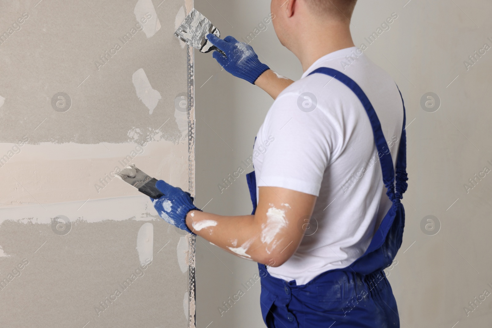 Photo of Man plastering wall with putty knife indoors, closeup. Home renovation