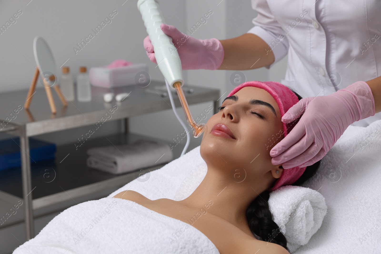 Photo of Young woman undergoing face rejuvenation procedure with darsonval in salon