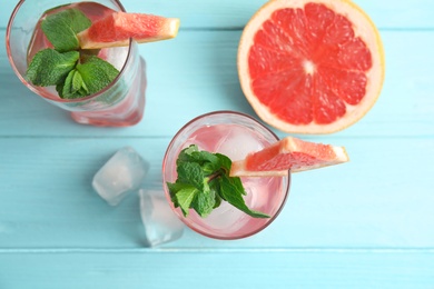 Photo of Glasses of grapefruit cocktails with ice on wooden table, flat lay