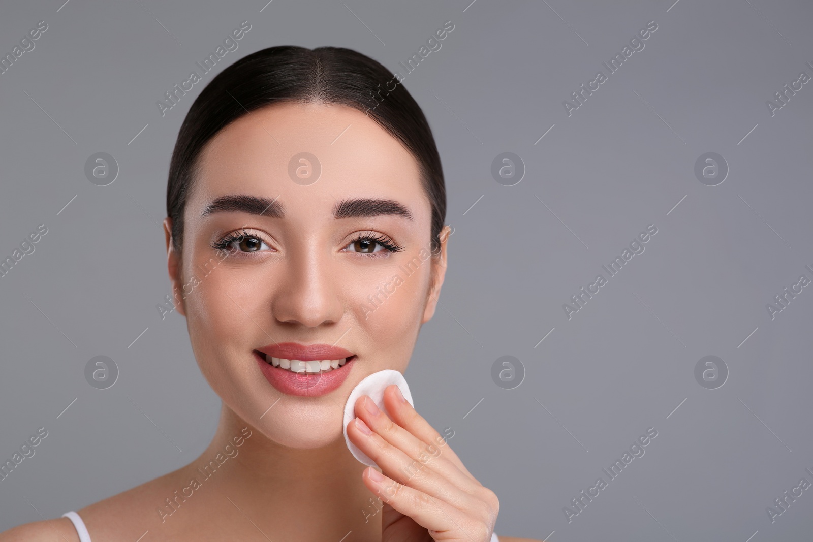Photo of Beautiful woman removing makeup with cotton pad on gray background, space for text