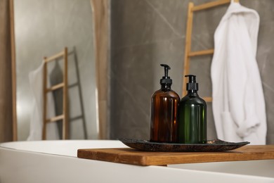 Photo of Wooden bath tray with bottles of shower gels on tub indoors, space for text