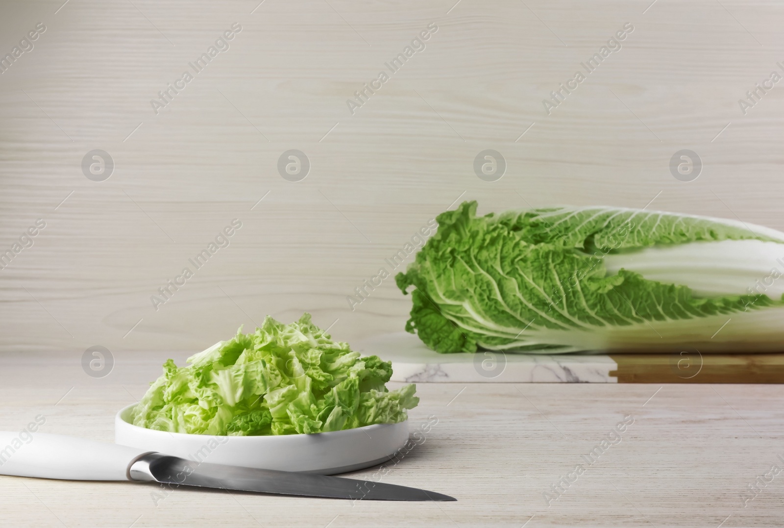 Photo of Whole and cut fresh ripe Chinese cabbage on table against white wooden background. Space for text