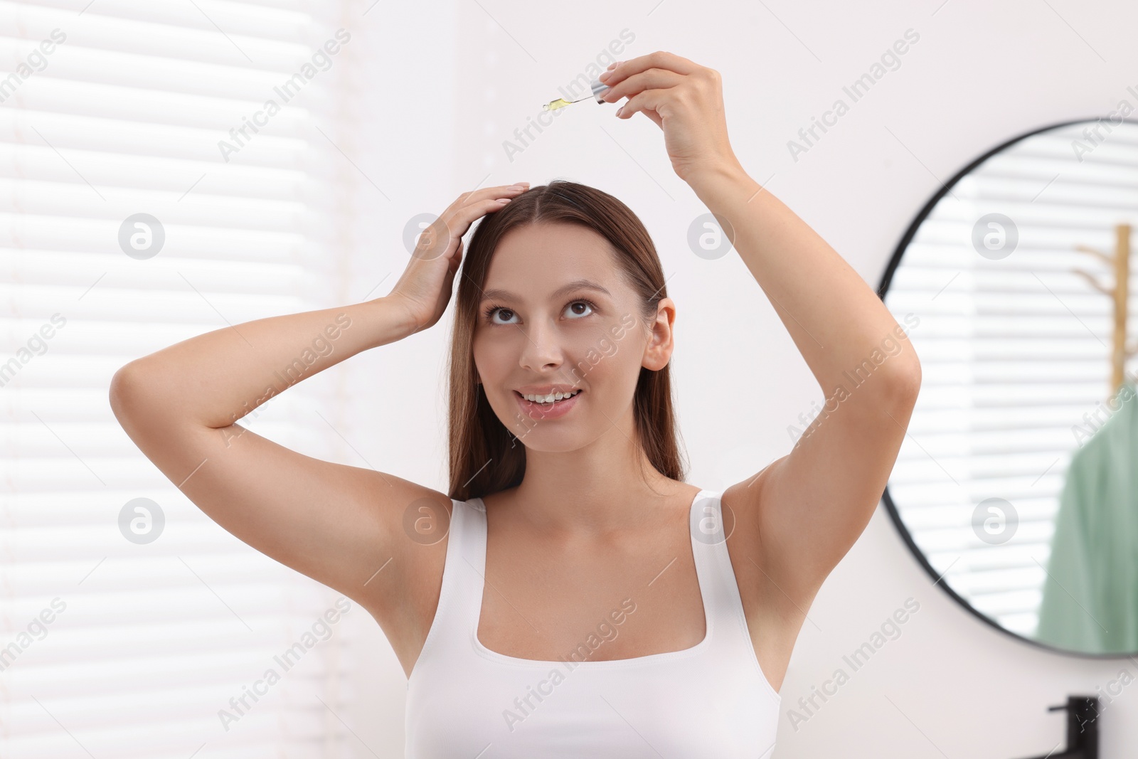Photo of Beautiful woman applying serum onto hair indoors