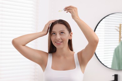 Beautiful woman applying serum onto hair indoors
