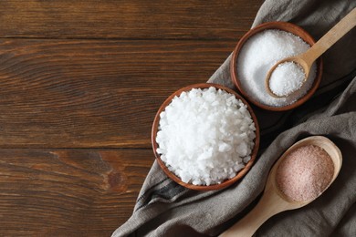 Photo of Different types of organic salt on wooden table, flat lay. Space for text