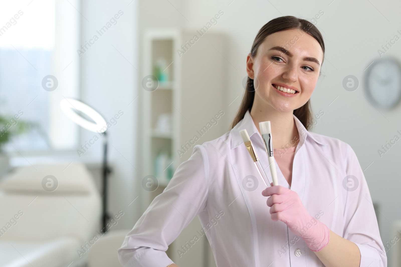 Photo of Cosmetologist with cosmetic brushes in clinic, space for text