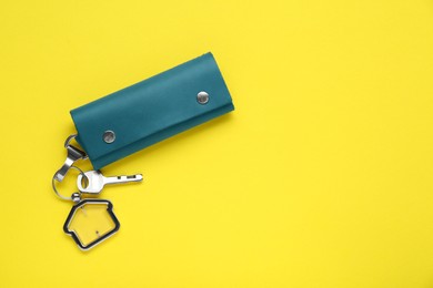 Photo of Leather case with key on yellow background, top view. Space for text