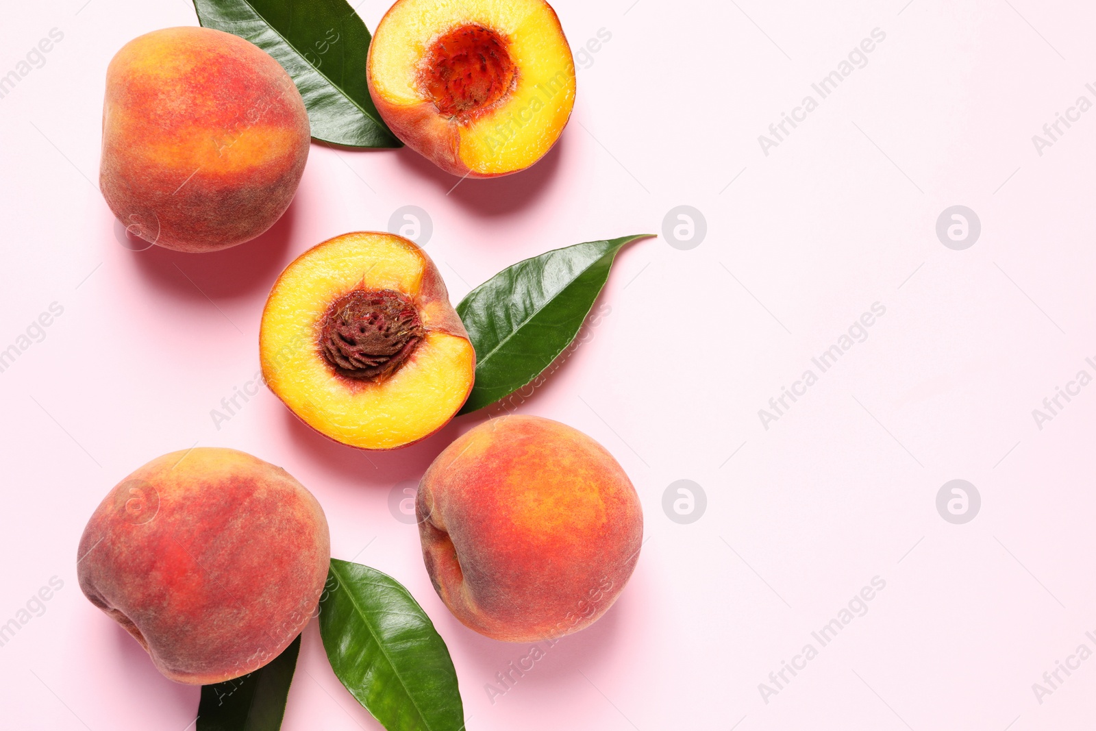 Photo of Cut and whole fresh ripe peaches with green leaves on pink background, flat lay. Space for text