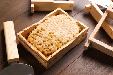 Photo of Honeycomb frame and beekeeping tools on wooden table, closeup