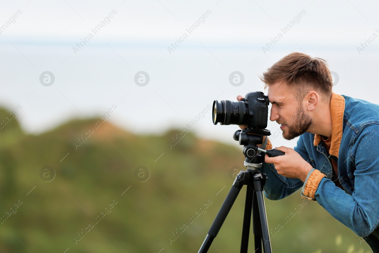 Photo of Male photographer taking picture of beautiful landscape with professional camera on green hill. Space for text