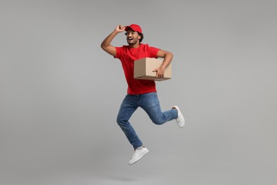 Photo of Happy young courier with parcel jumping on grey background