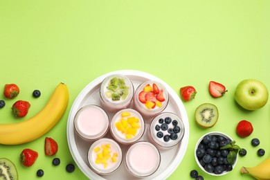 Photo of Yogurt maker with jars and different fruits on light green background, flat lay. Space for text