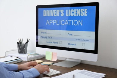 Photo of Man using computer to fill driver's license application form at table in office, closeup