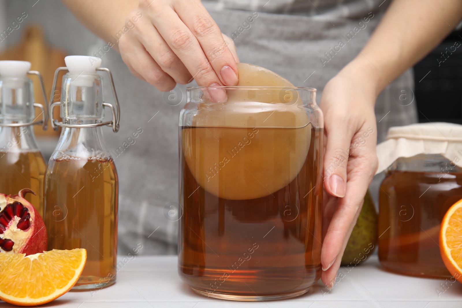 Photo of Woman making homemade fermented kombucha at white table, closeup