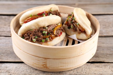 Delicious gua bao in bamboo steamer on wooden table, closeup
