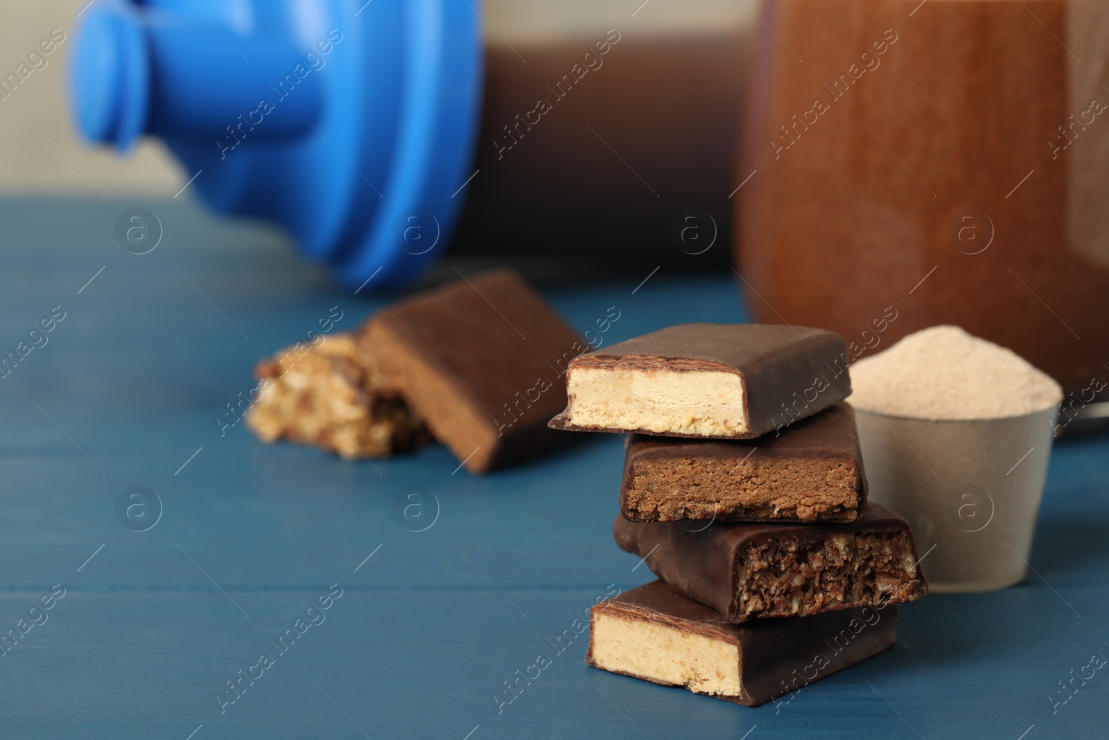 Photo of Different energy bars, protein cocktail and powder on blue wooden table. Space for text