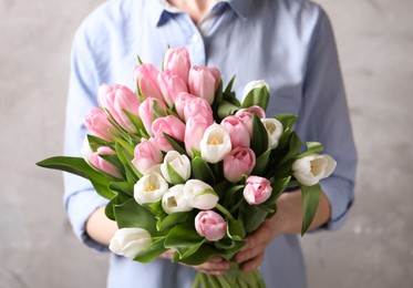 Photo of Woman holding bouquet of tulips against beige background, closeup