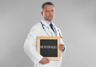 Photo of Doctor holding blackboard with word HEMORRHOID on light grey background