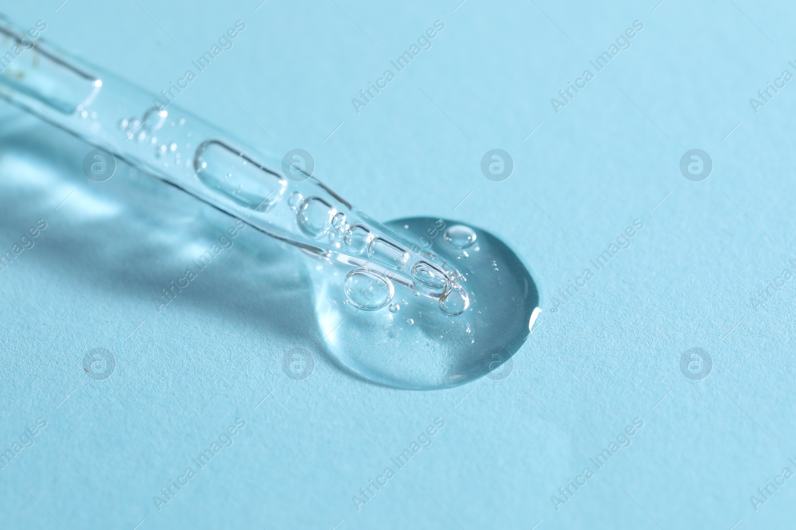 Photo of Glass pipette and transparent liquid on light blue background, closeup