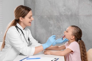 Photo of Doctor taking throat swab sample from girl`s oral cavity indoors