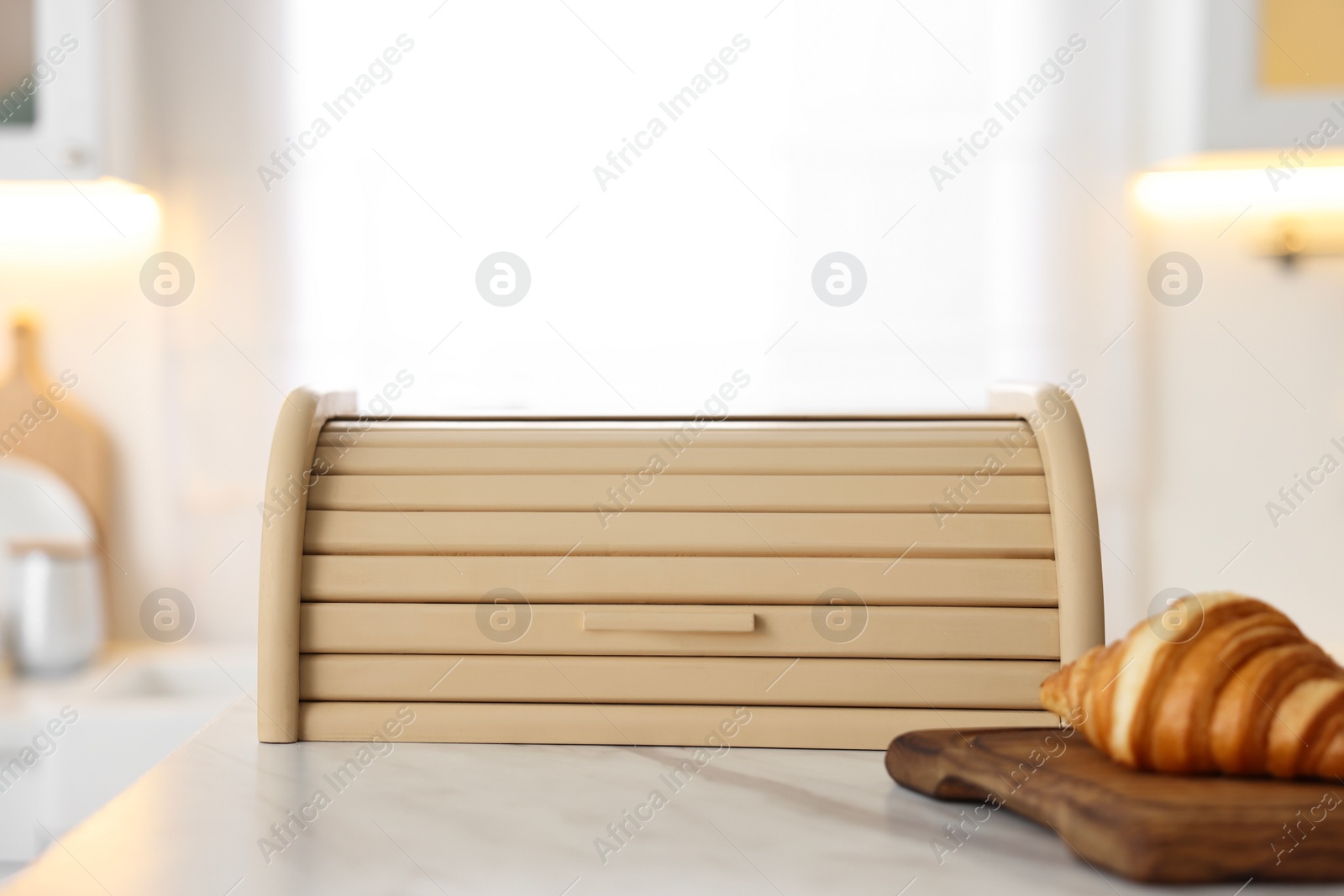 Photo of Wooden bread box and board with croissant on white marble table in kitchen