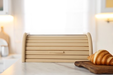 Wooden bread box and board with croissant on white marble table in kitchen