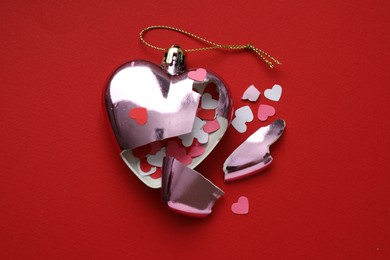 Photo of Crashed bauble in shape of heart with confetti on red background, top view. Broken heart