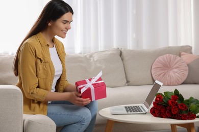 Photo of Valentine's day celebration in long distance relationship. Woman holding gift box while having video chat with her boyfriend via laptop at home