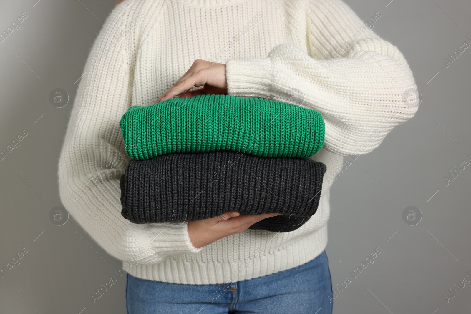 Photo of Woman with stack of knitted sweaters on grey background, closeup