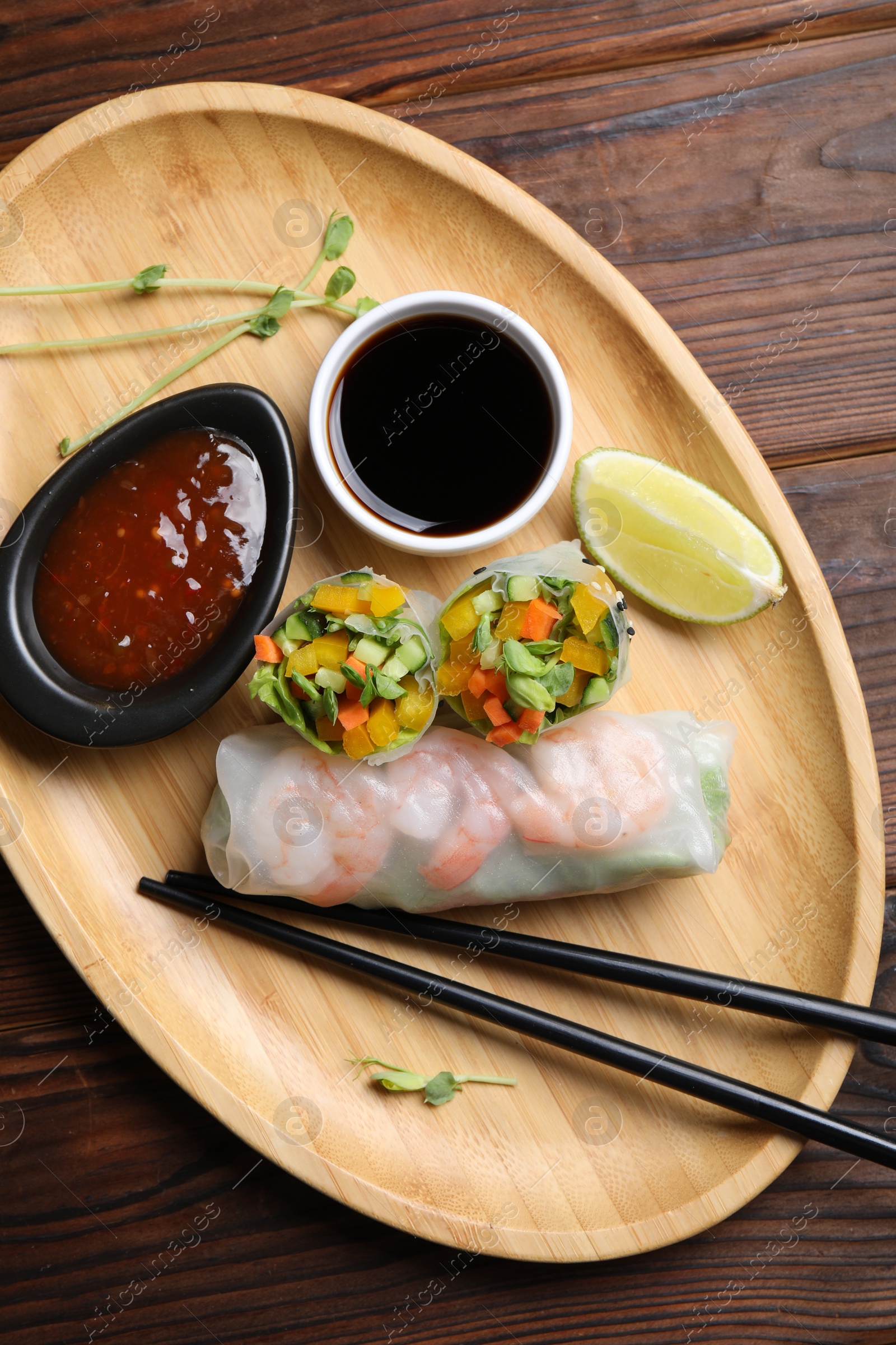 Photo of Tasty spring rolls and sauces on wooden table, top view